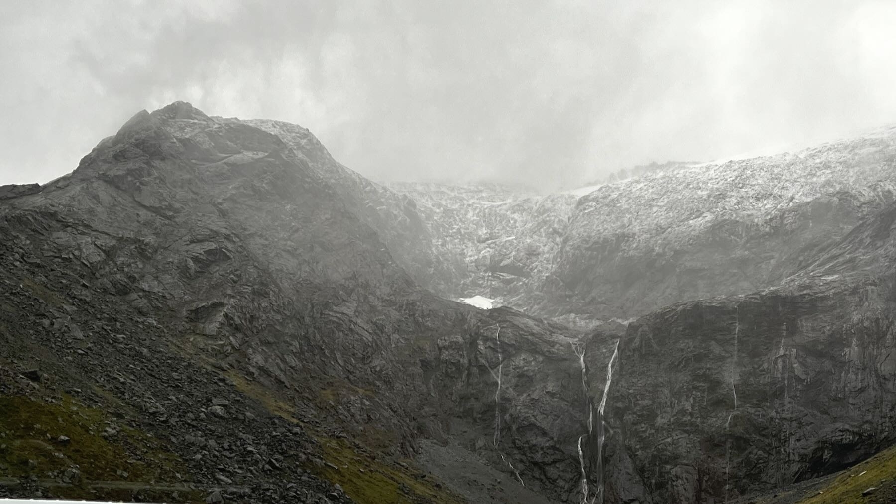Bare snowy mountain tops with streams. Above, misty rain.