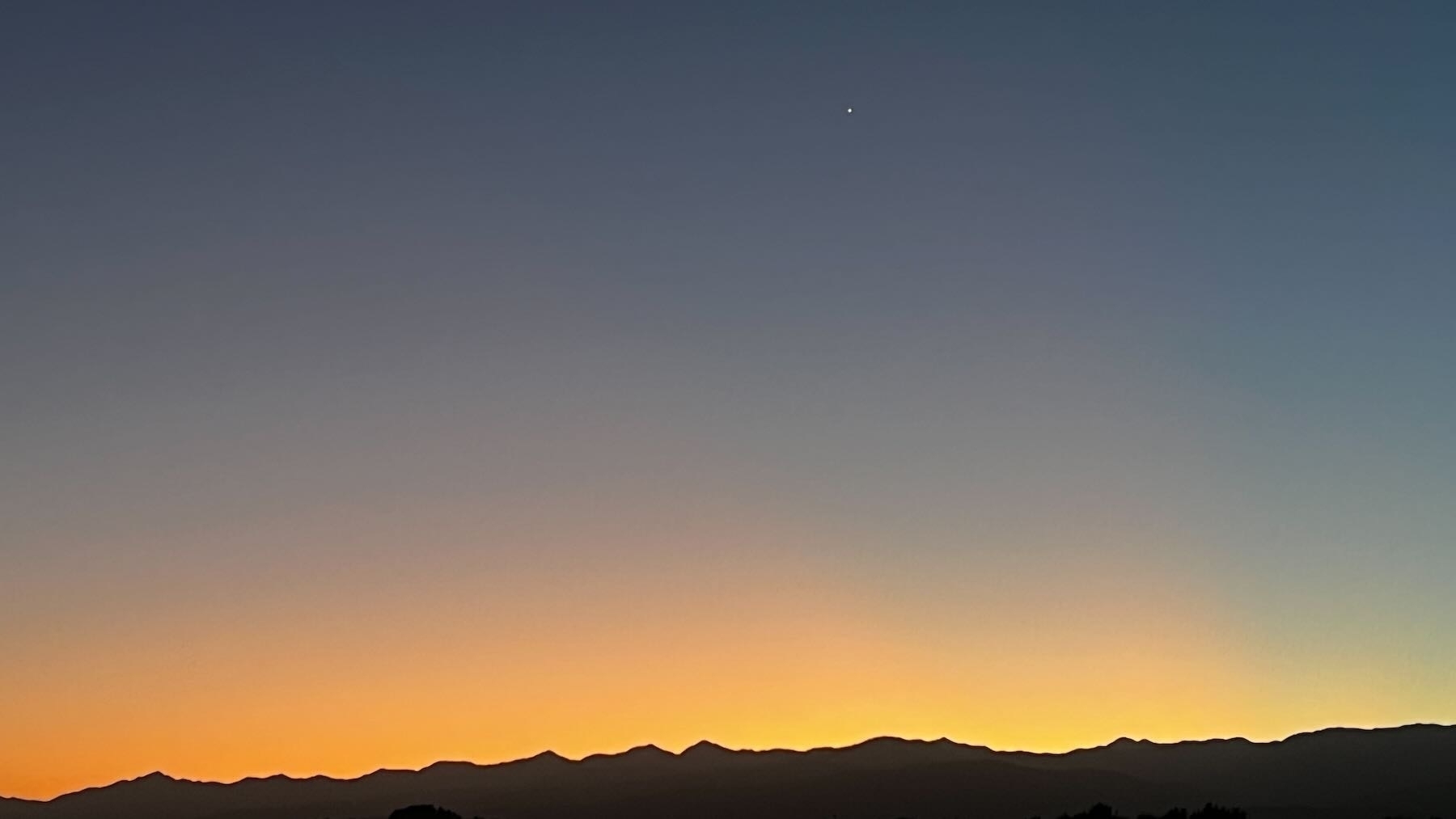 Dark hills at the borrom of the shot with sunrise peach sky above then Venus higher in the darker sky. 