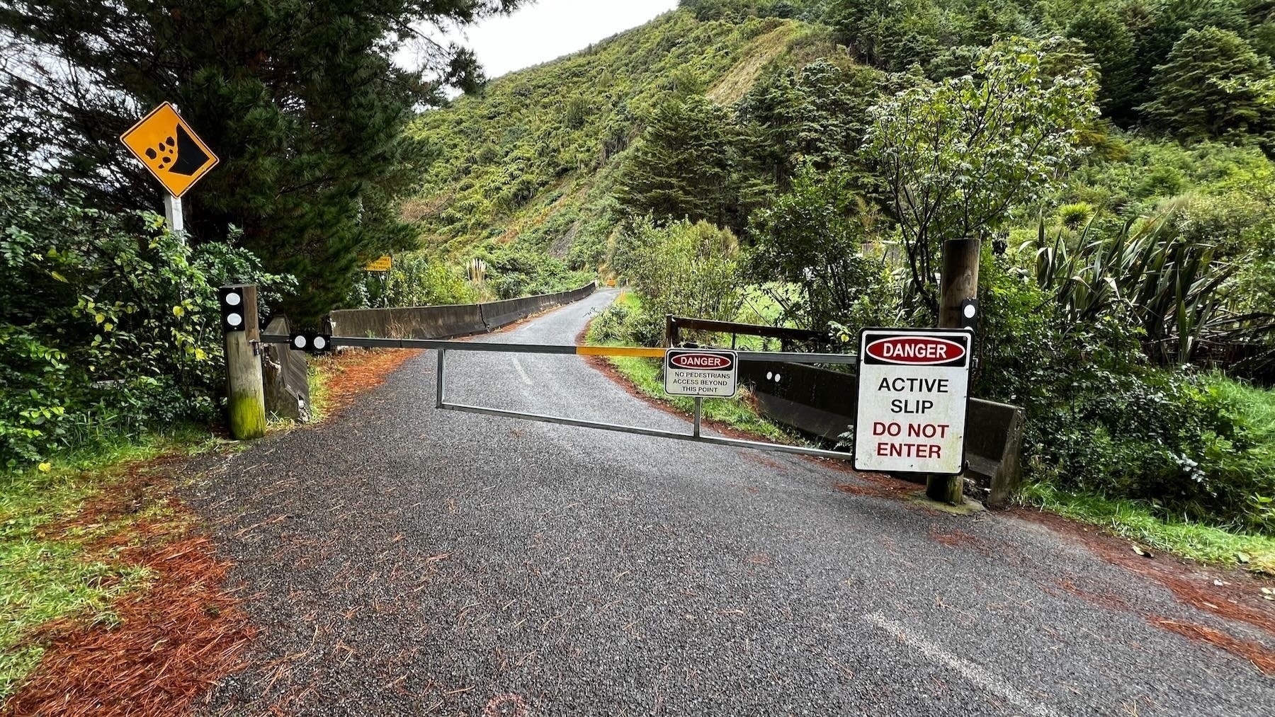 Ōtaki Forks walk, road closed barrier and signage. Lush green hills behind. 