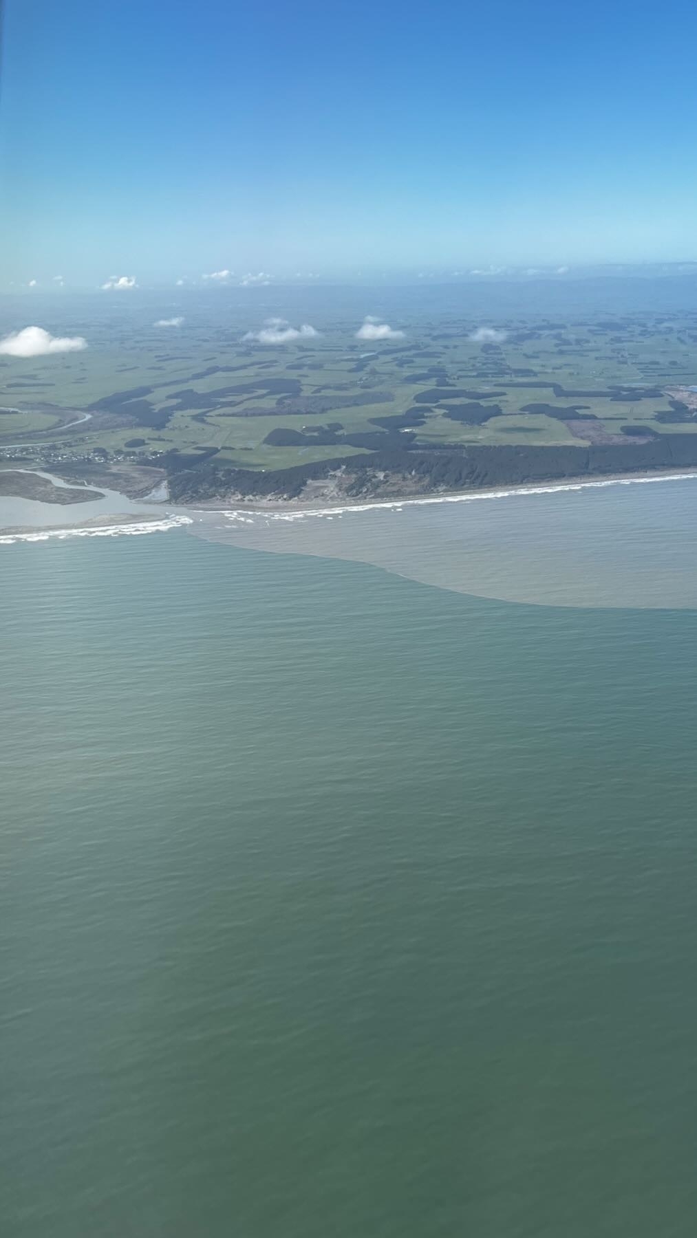 A river mouth where the outflowing water is grey and muddy, against a sharp line of blue green sea. 