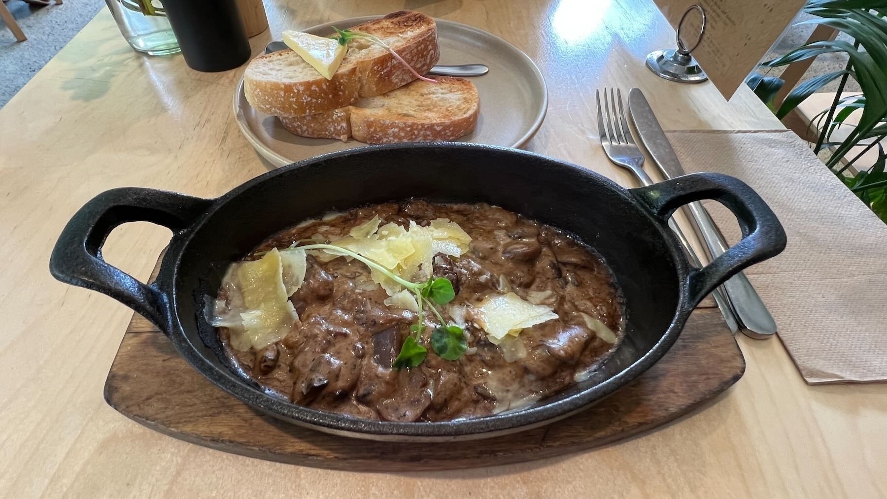 A mushroom dish on a hot black iron plate, with toast on a separate plate nearby. 