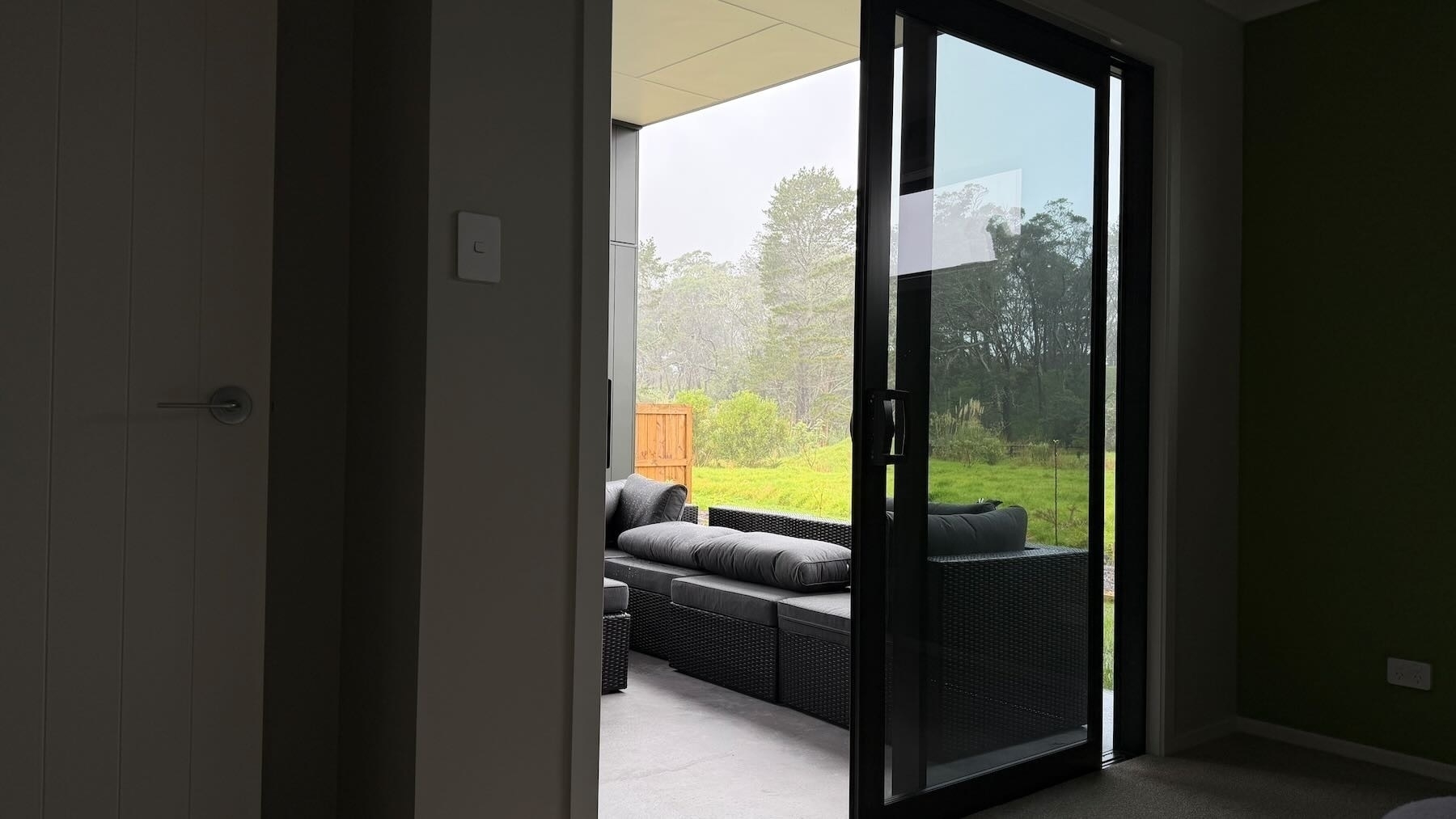 A 1x view through a window, across a patio and green grass to tall trees about 100 metres away.