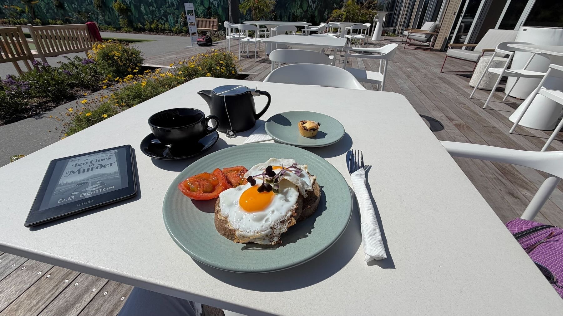 A plate of eggs on toast with tomato, a Kindle, a pot of tea and a mince tart.