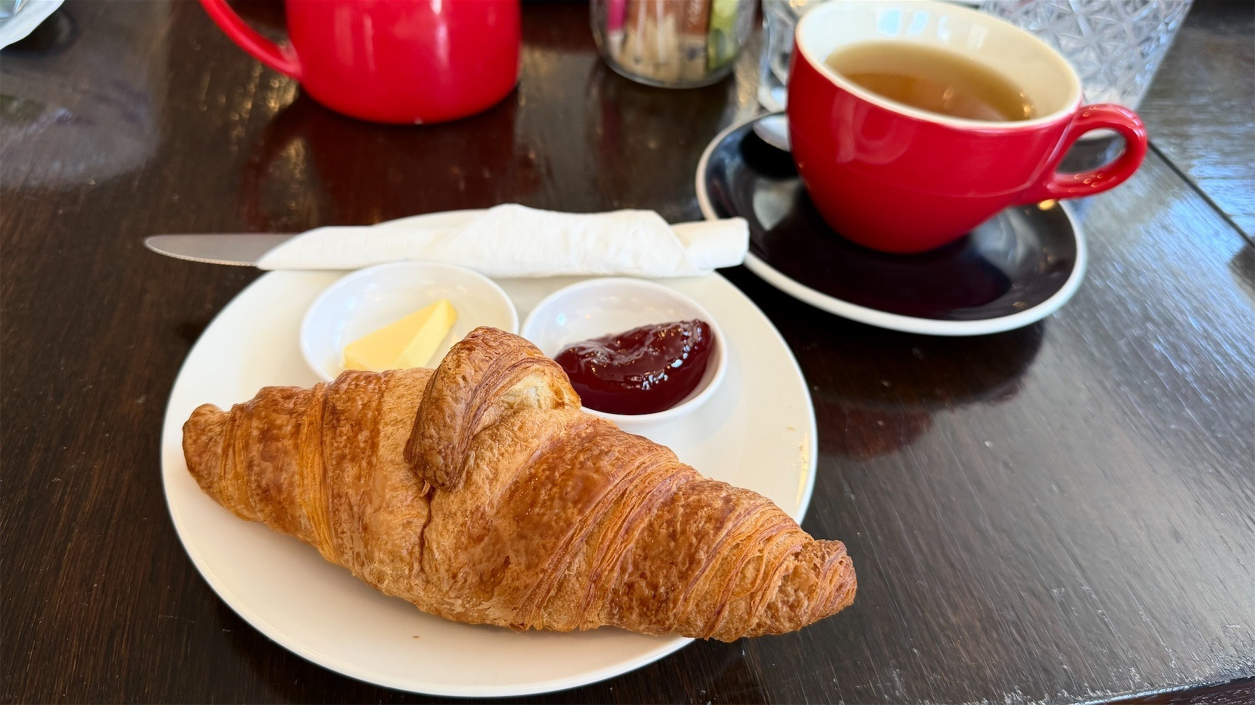 Croissant on a plate with butter and jam, and a cup of tea. 