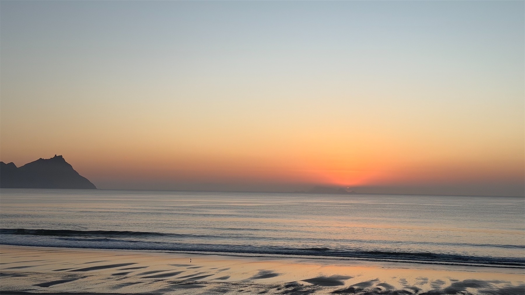 Quiet sea, distant hills, dark cloud on the horizon, red where the sun will rise in a moment. 