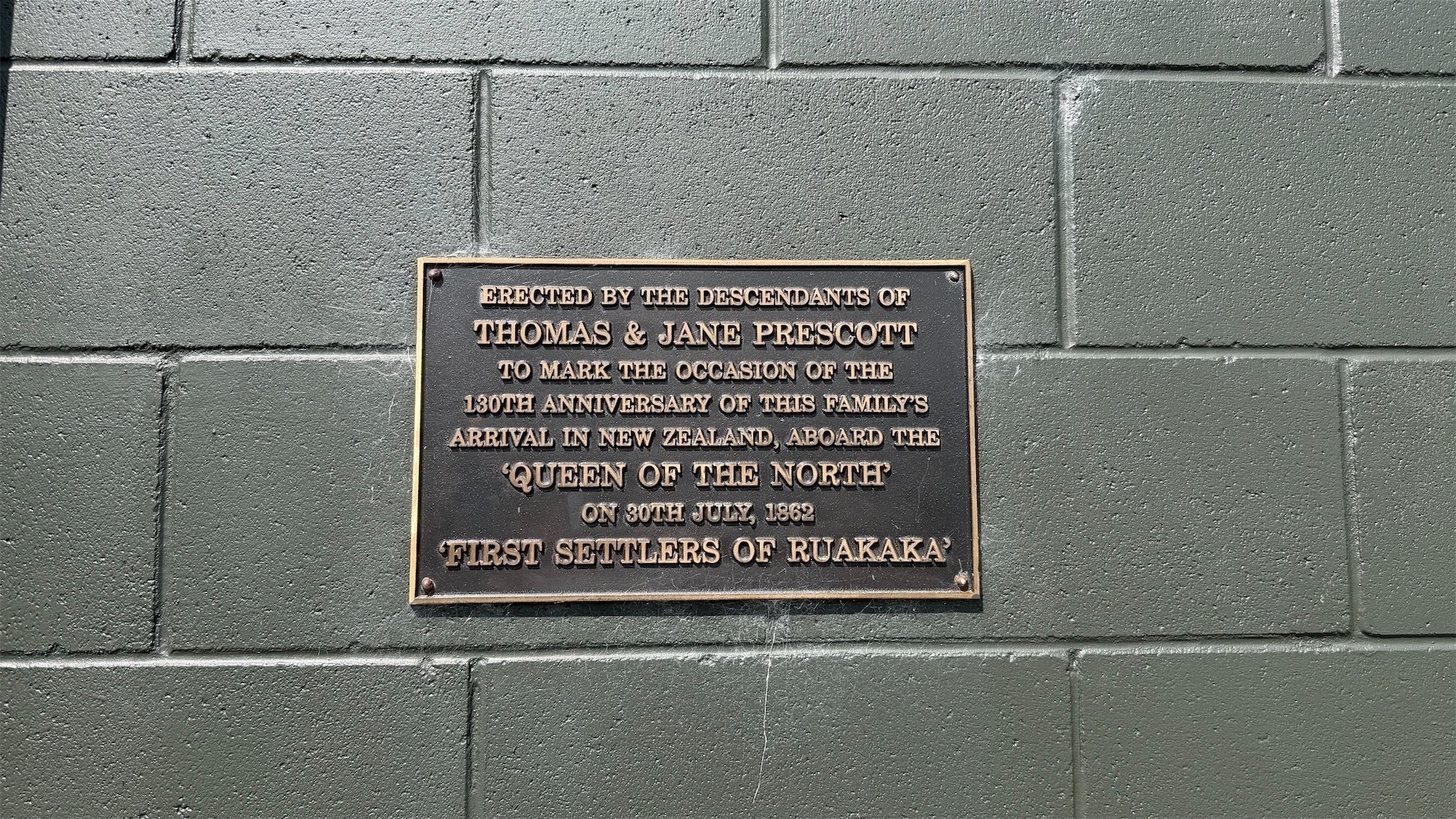 A plaque on a brick wall reads: Erected by the descendants of
Thomas & Jane Prescott to mark the occasion of the 130th anniversary of this family's arrival in New Zealand, aboard The 'Queen Of The North on 30th June, 1862 First Settlers Of Ruakaka.