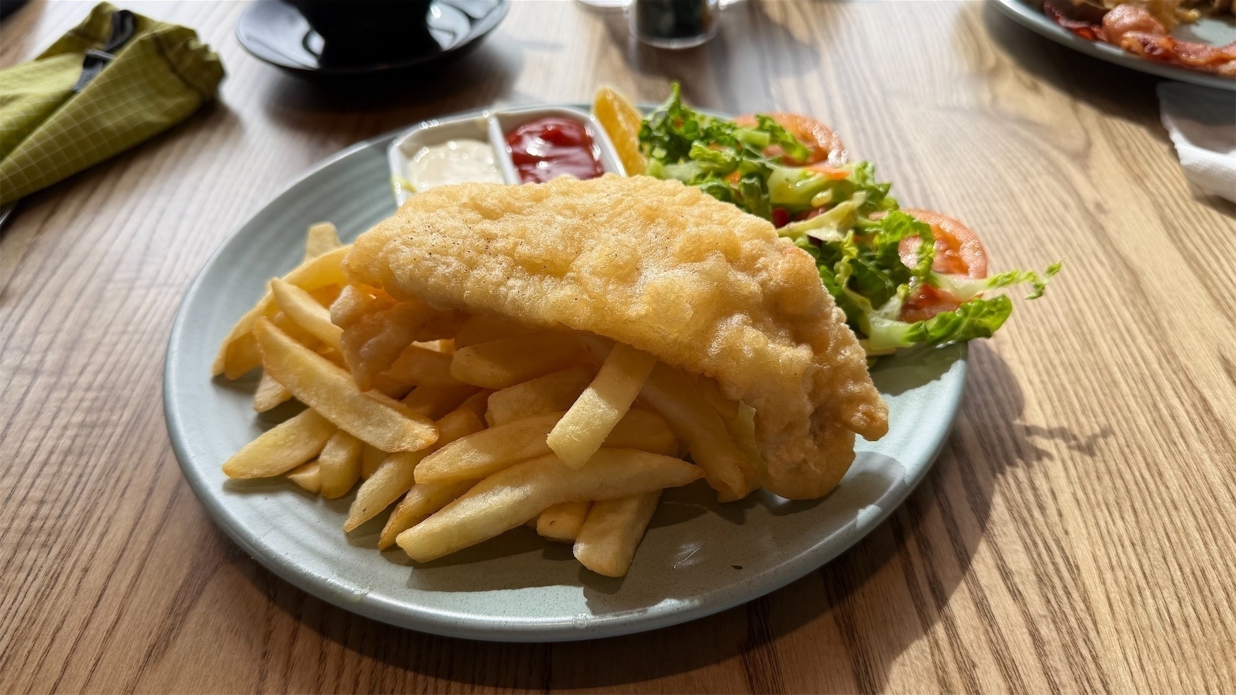 A plate of fish and chips with salad and dressings.