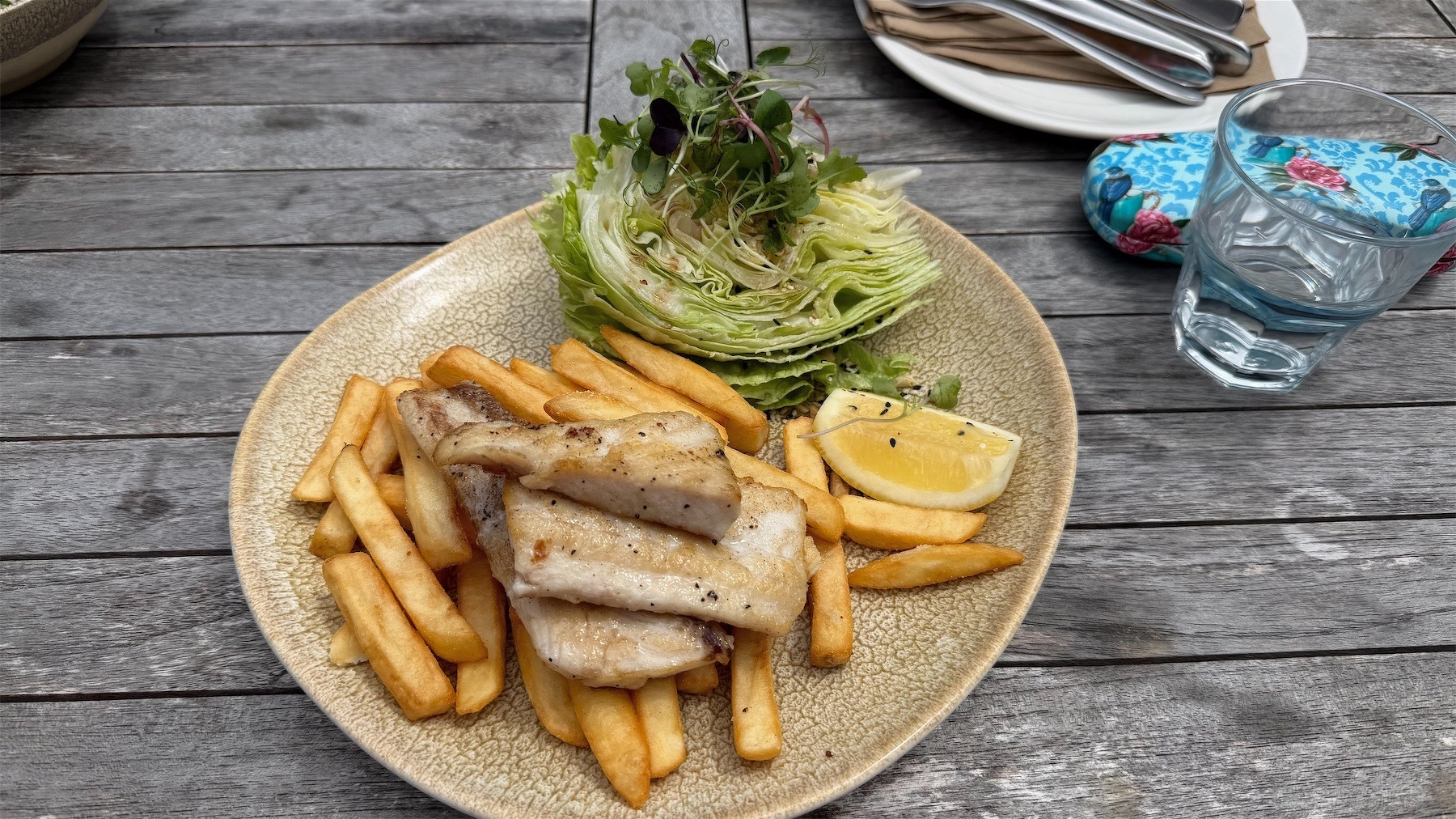 A plate of chips with several part fillets of fried fish on top and a large wedge of iceberg lettuce.