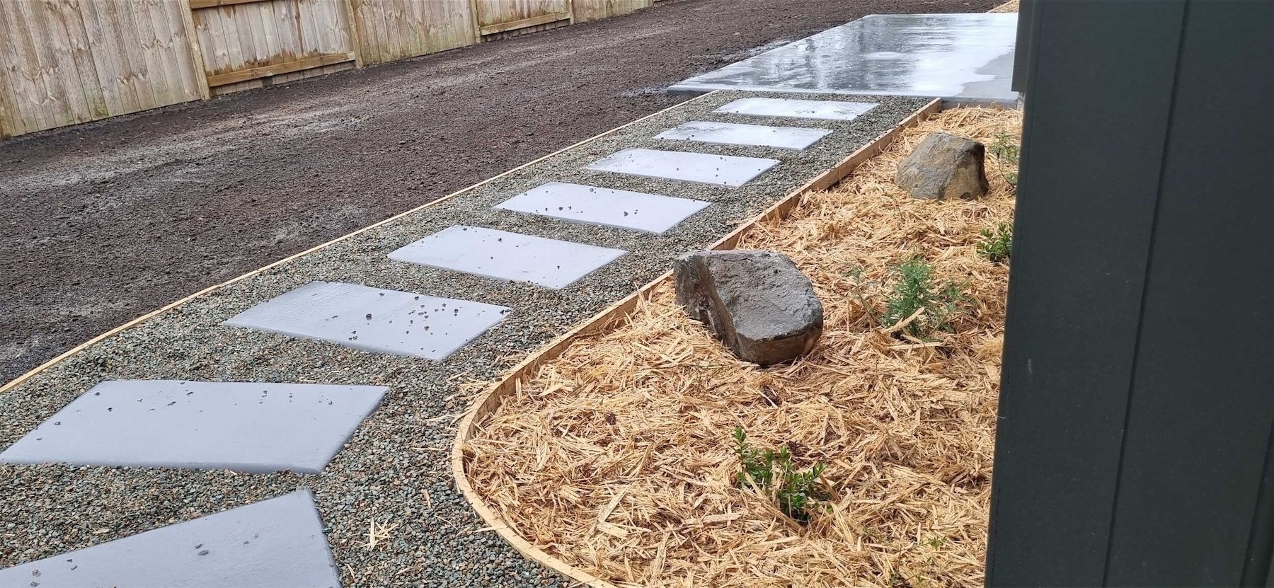 A section of curved path with concrete pavers in a bed of shingle, with a small mulched area of garden to one side.