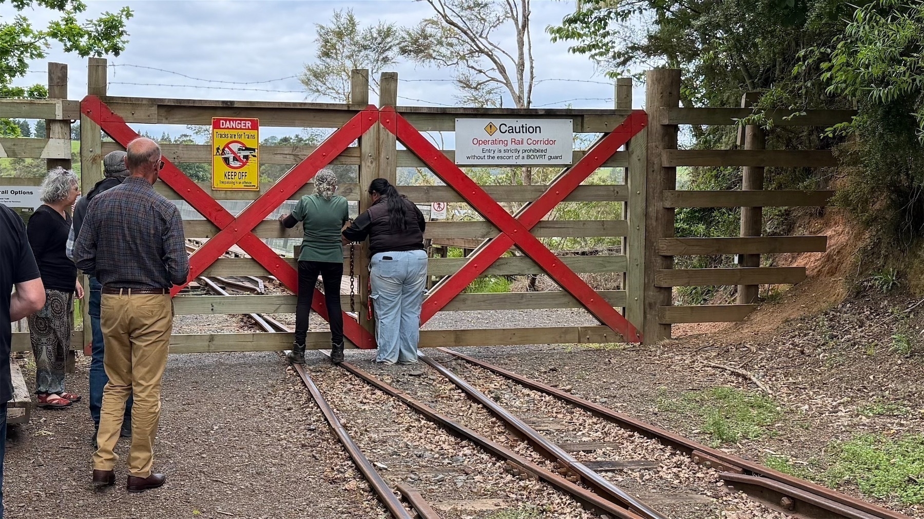 Two women open large gates so the train can pass through to the curved wooden bridge. 