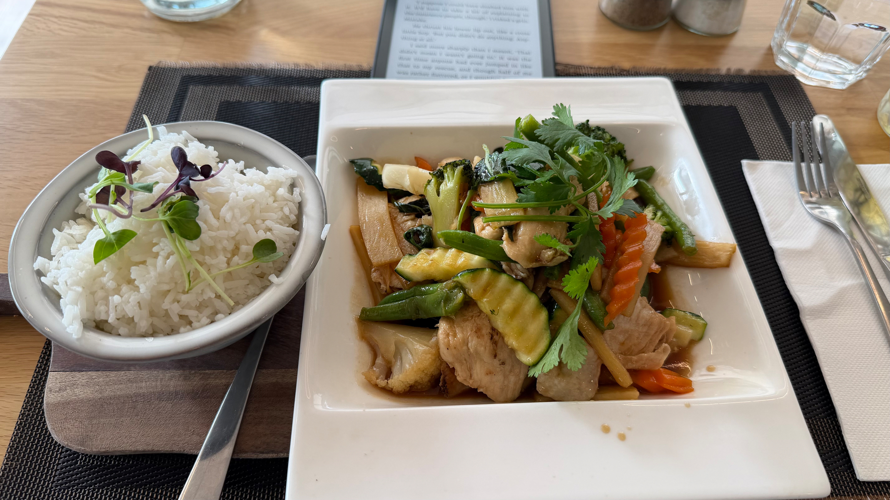 A dish of stir-fried vegetables and chicken is served alongside a bowl of steamed rice garnished with microgreens.