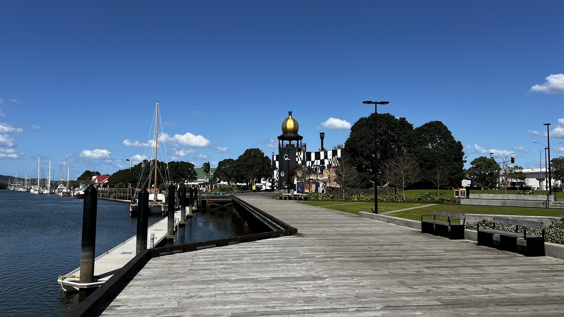 A waterfront promenade features a boardwalk, docked boats, and a unique building with a gold dome and checkerboard pattern.