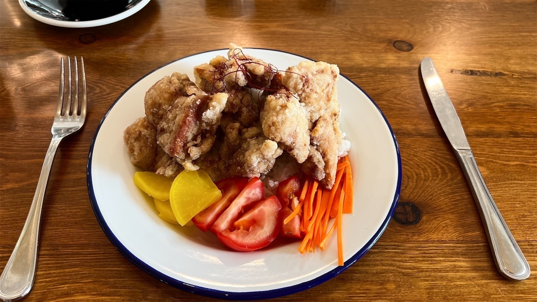 Korean fried chicken heaped on rice, with daikon, carrot julienne and tomato quarters, all on an enamel plate.