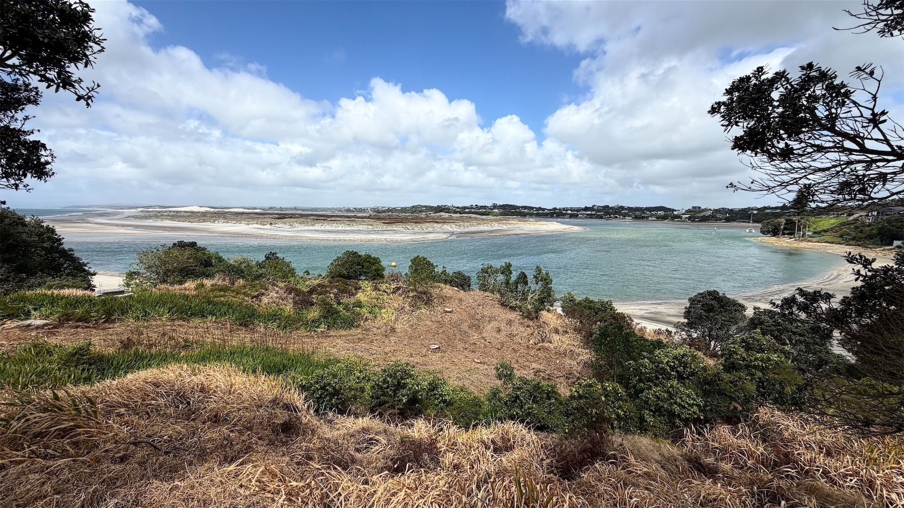 Panorama of a hillside looking over beach, sea and a sandspit. 