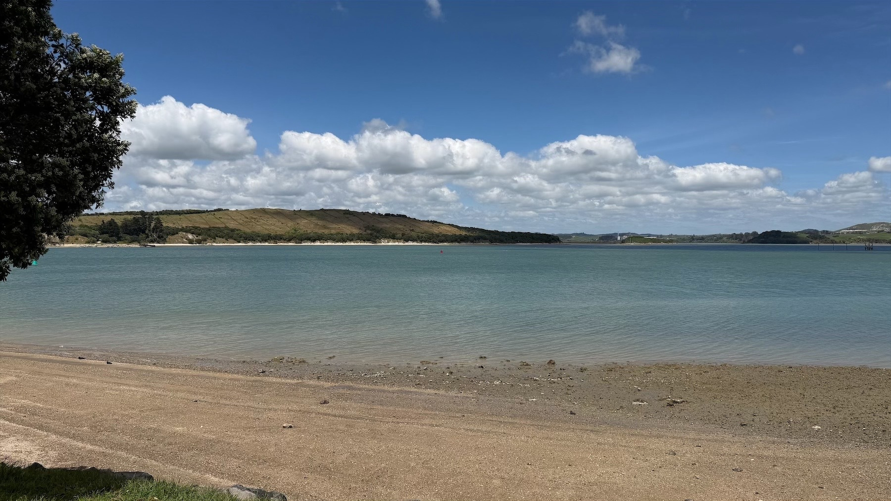 View across golden sand and water to hills on the other side of the harbour. 