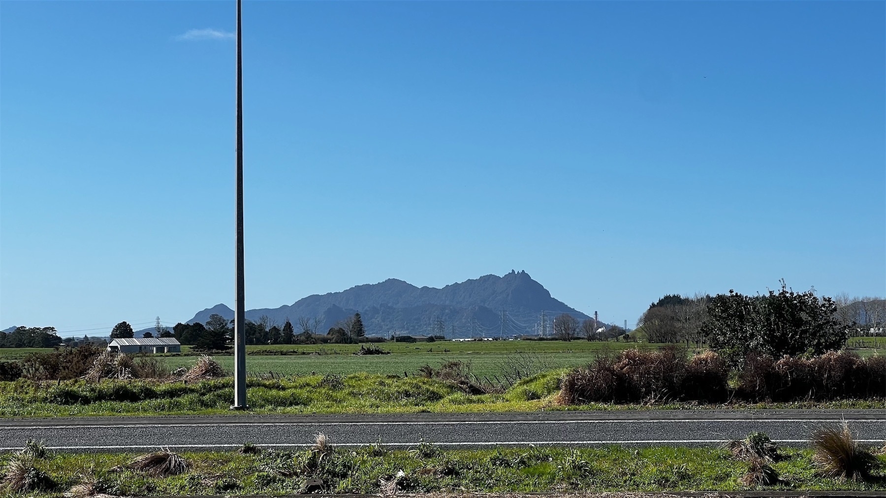 View across a road and paddocks towards a mountain with clear crisp blue sky behind it.
