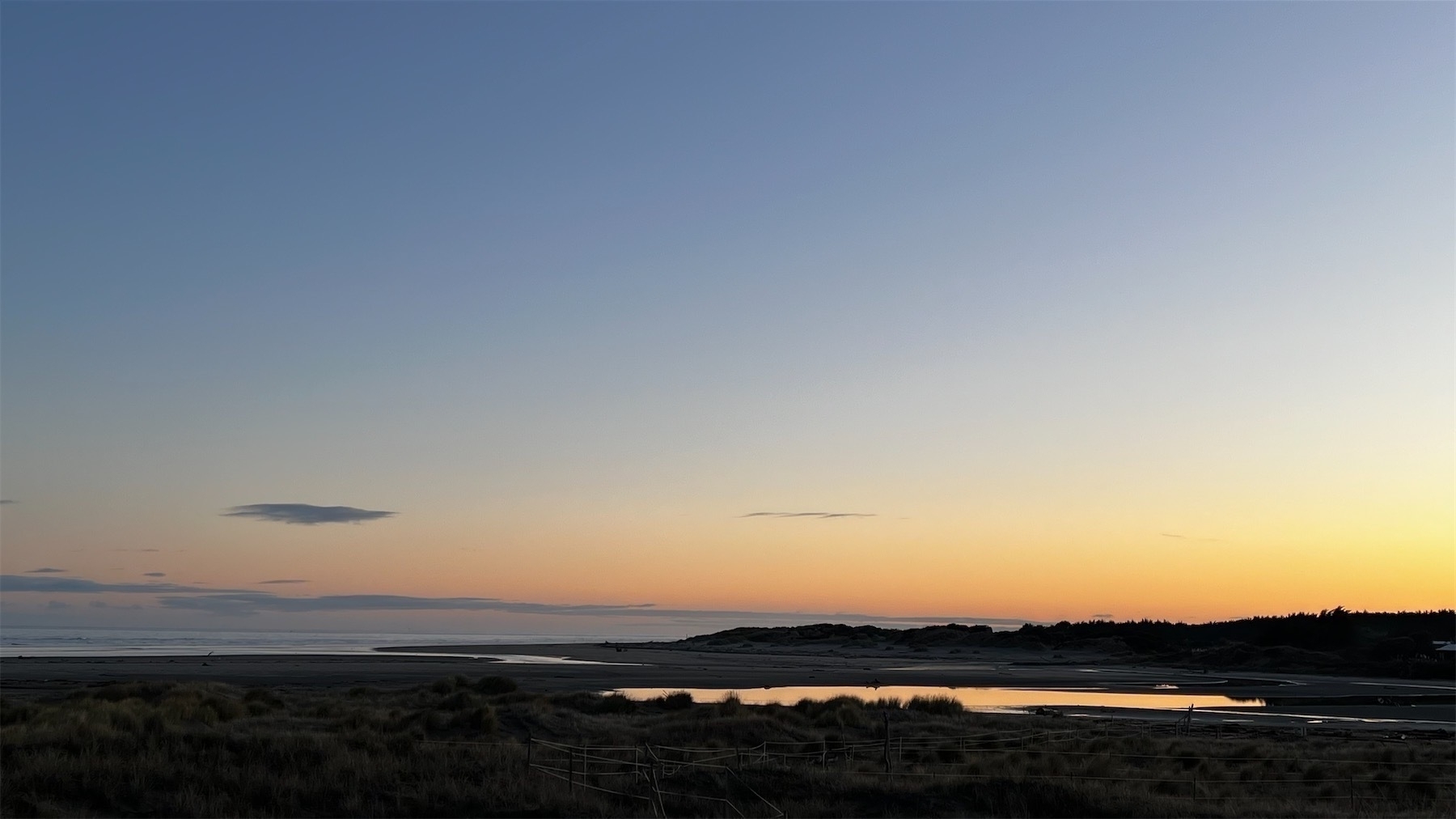 Pre-dawn sky with a patch of shining water on dark land below. 