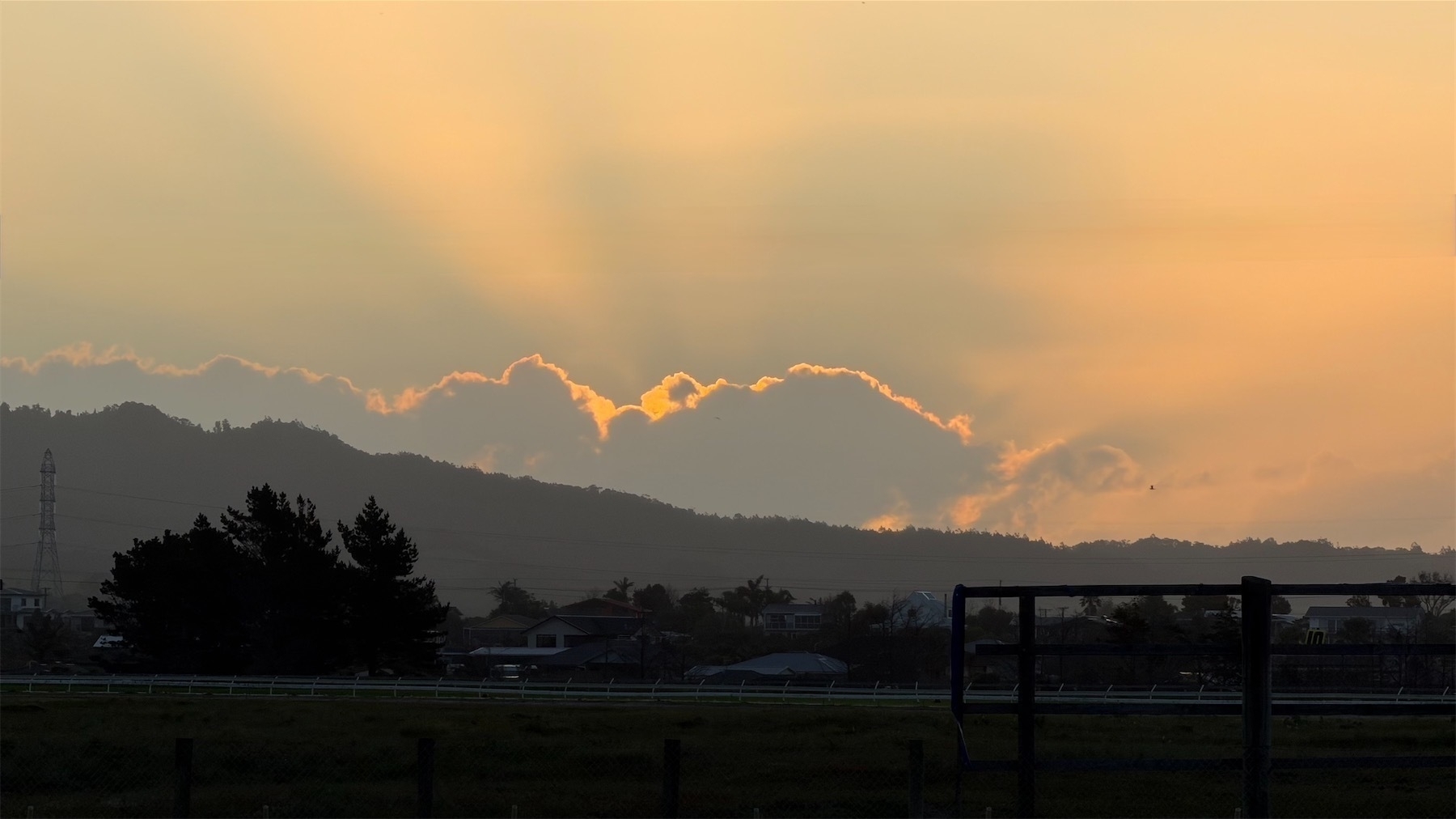 A darkened landscape with backlit billowy clouds and rays of sunshine escaping behind. 