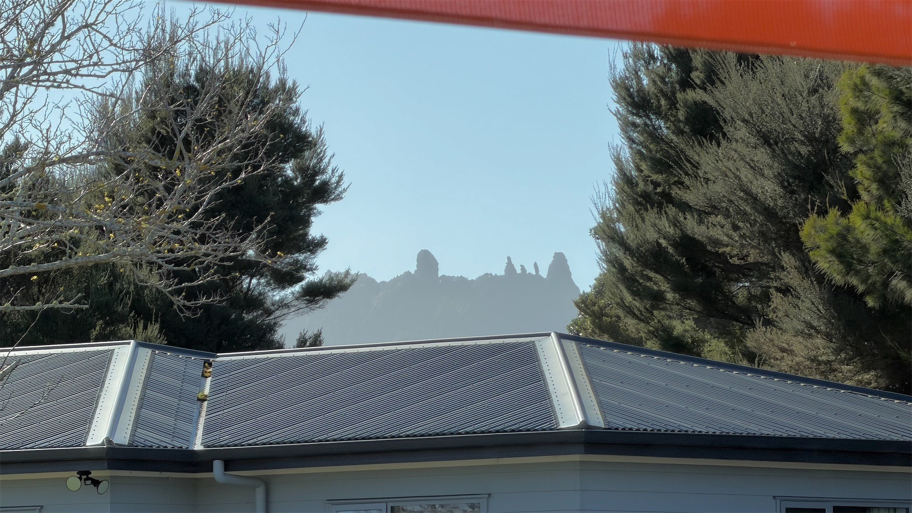 Craggy mountain framed between a house roof, trees and an awning.