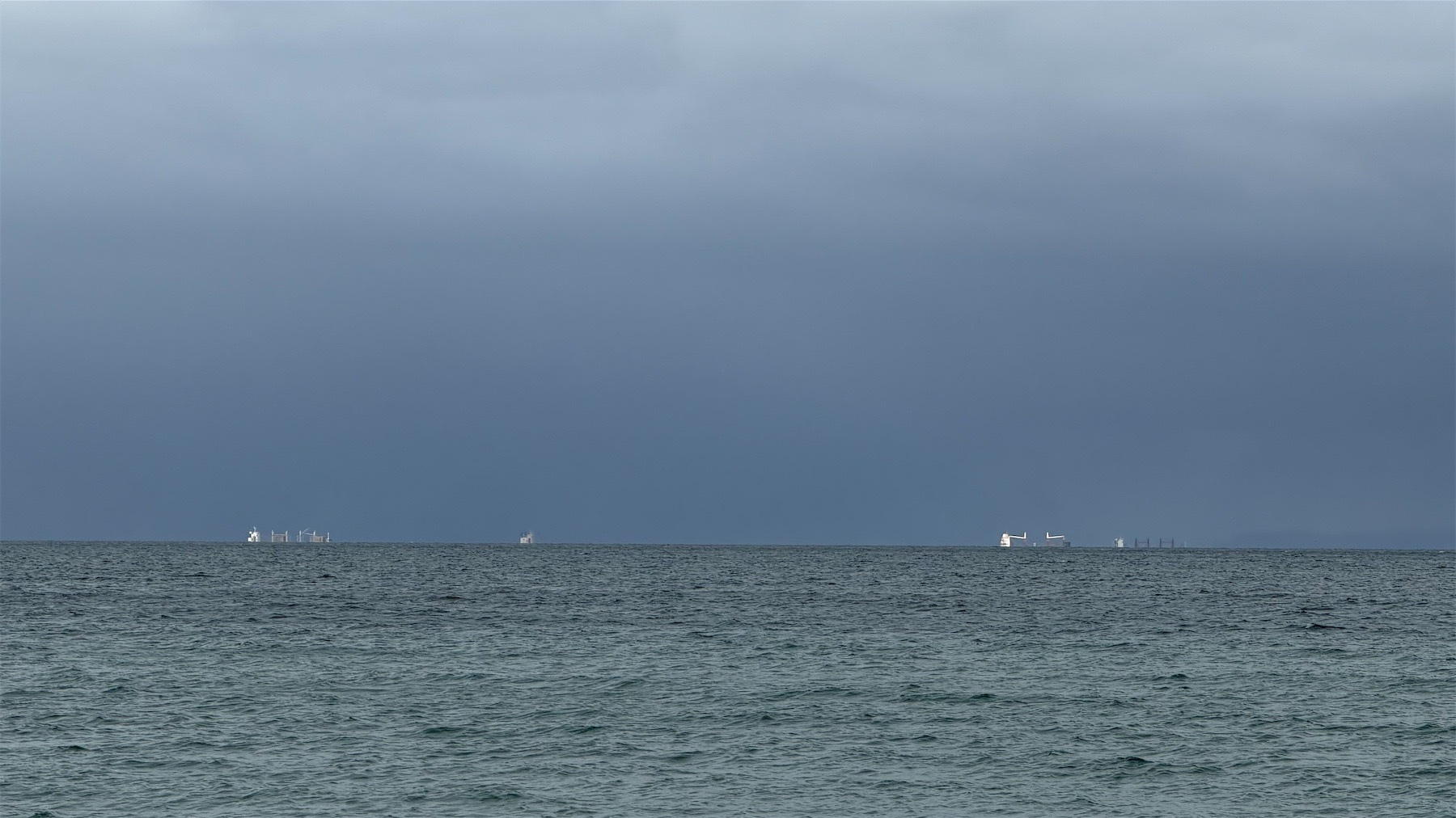 4 ships shine white against dark sky and grey sea.