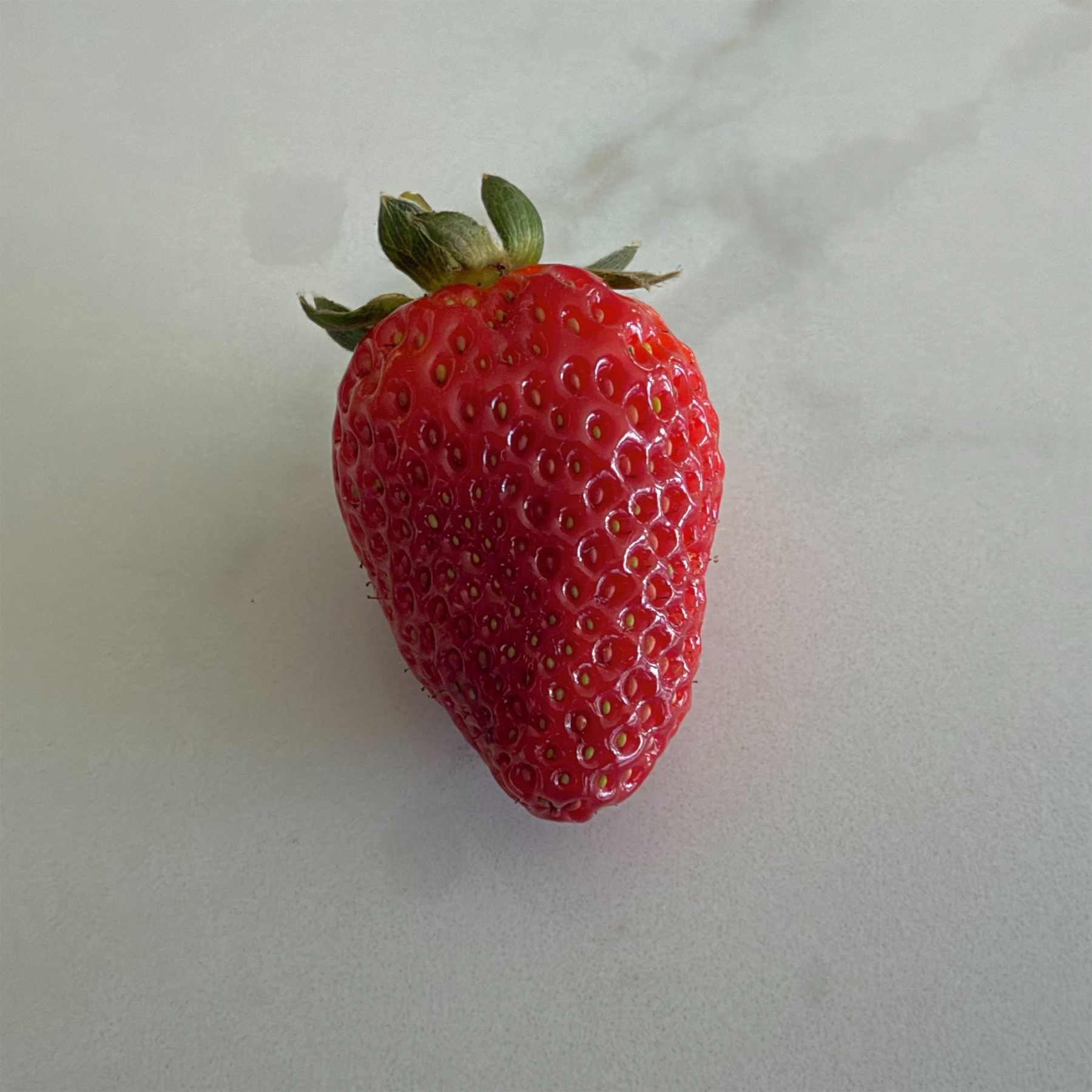 A ripe red strawberry on a bench top.