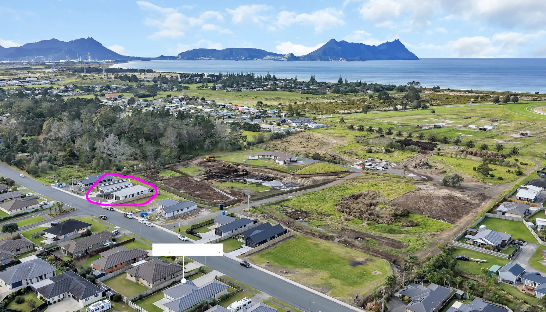 Aerial photo of houses in streets and a big open area being worked on with heavy machinery. In the near distance is the coast.