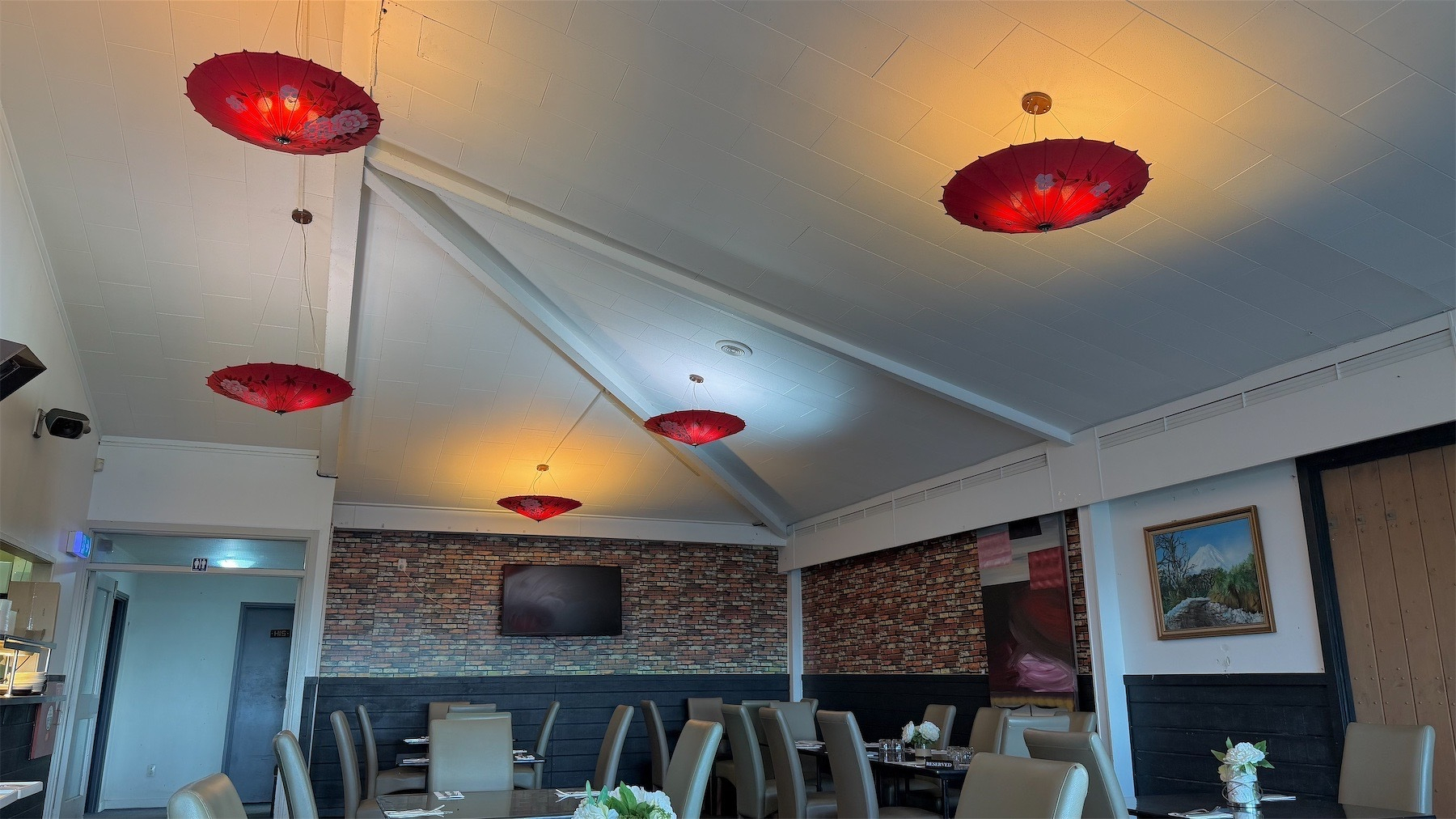 Red umbrellas screen overhead lights, tables, chairs and brick-style walls.