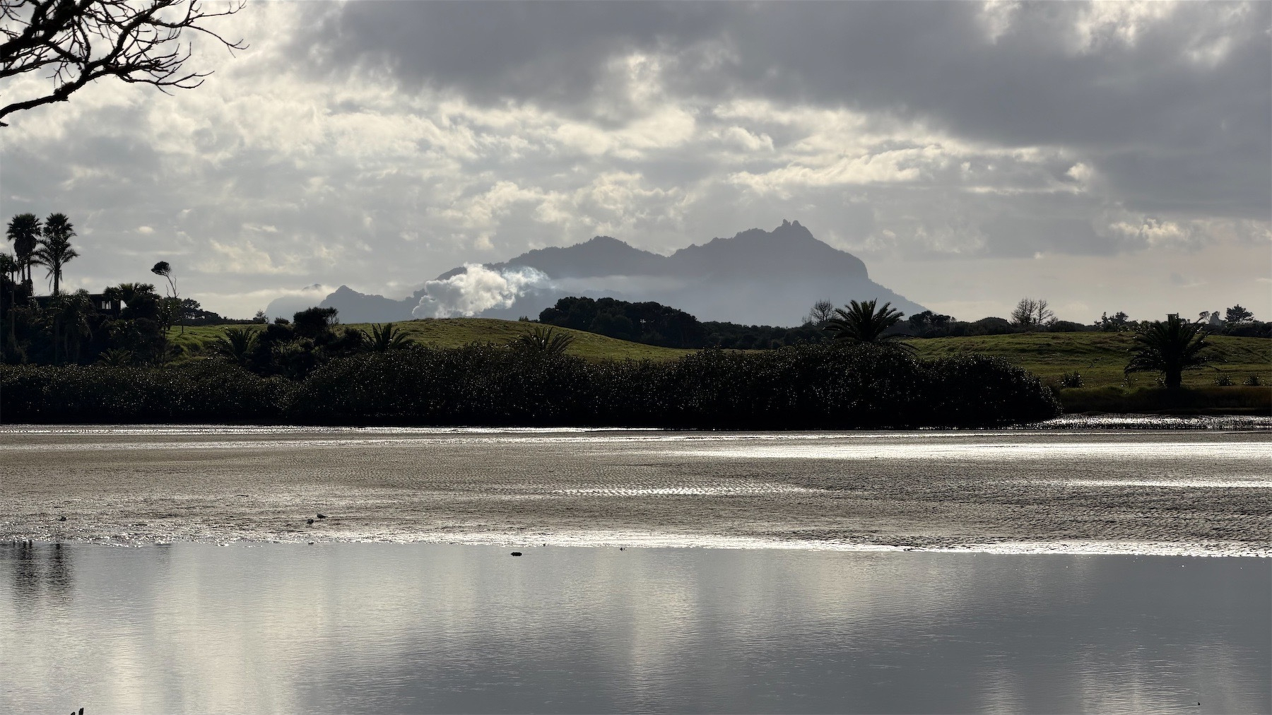 Mt Manaia in the distance with greenery in mid-ground and calm water in foreground.