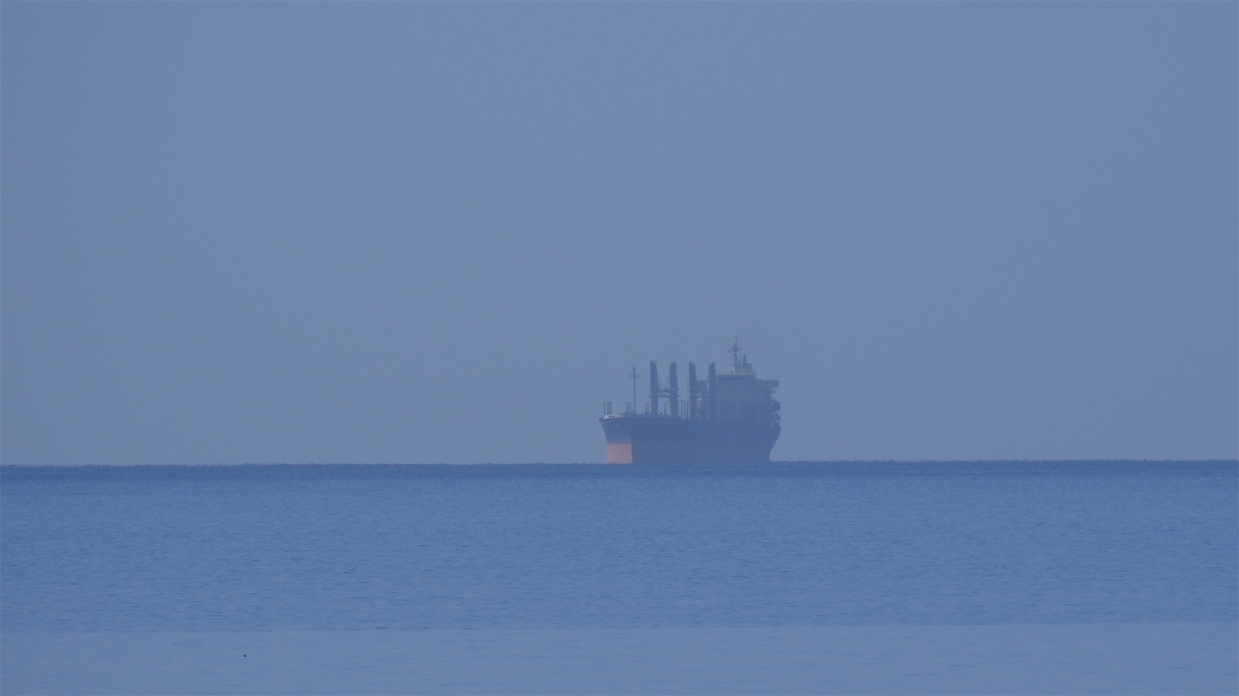 Hazy view of a ship on the horizon, caught between sea and sky.