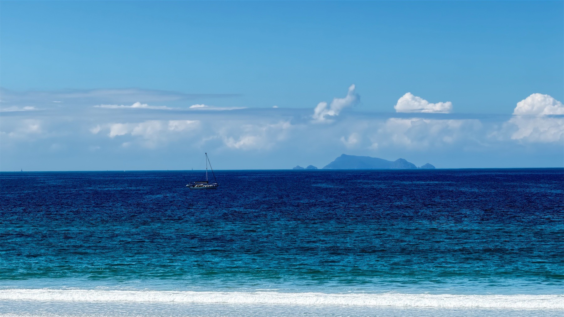 Sailboat near shore, with an island in the background.
