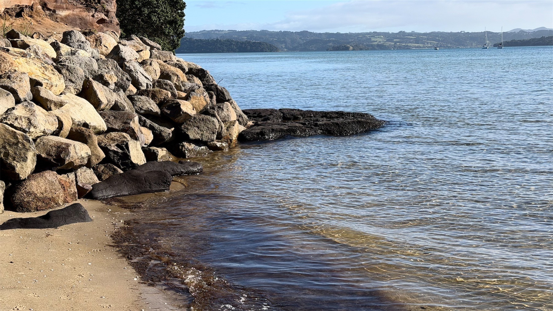 An apron of black rock is surrounded by water, with boulders to one side.