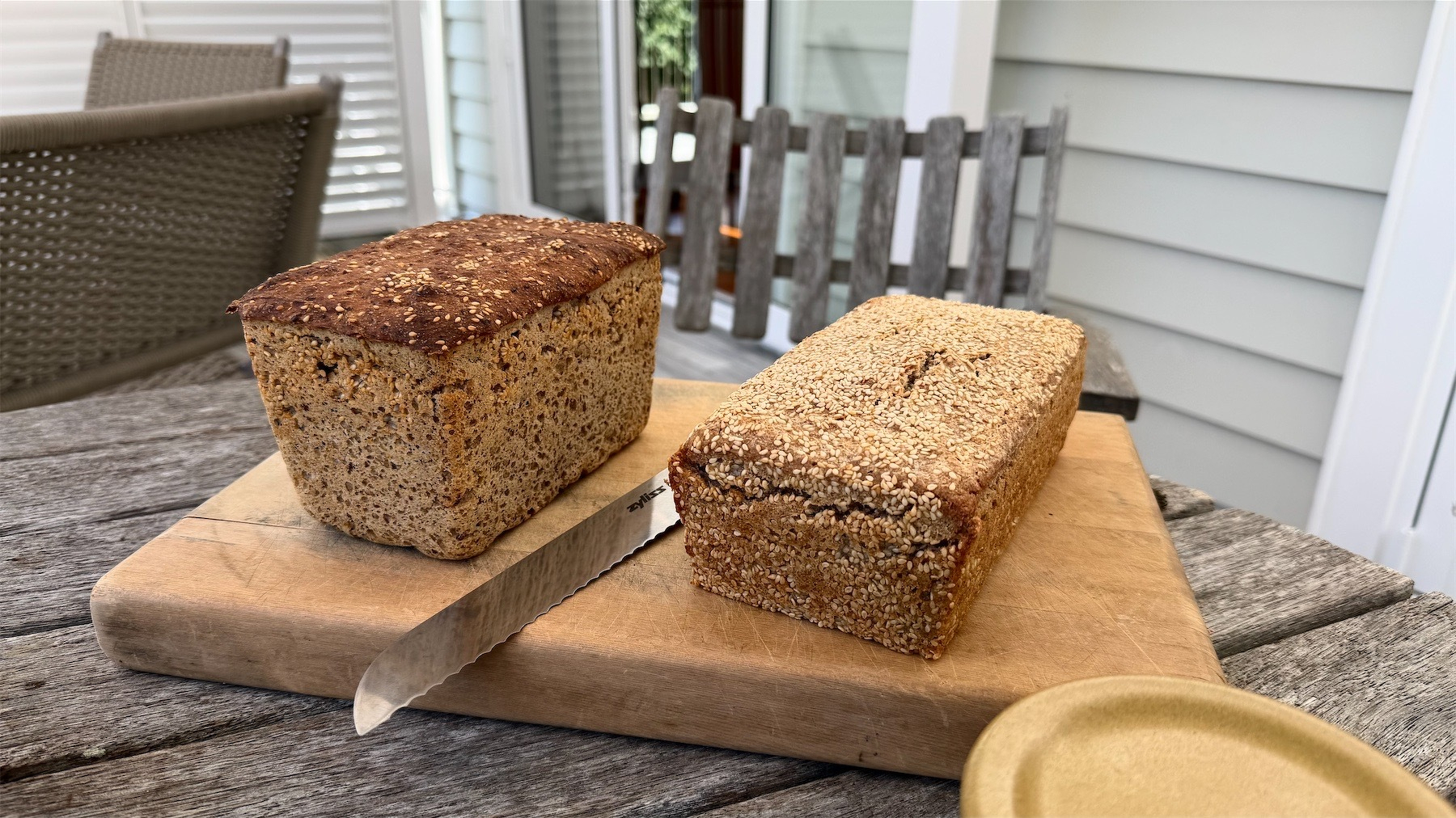 Two loaves of bread on a wooden cutting board, with a large knife.