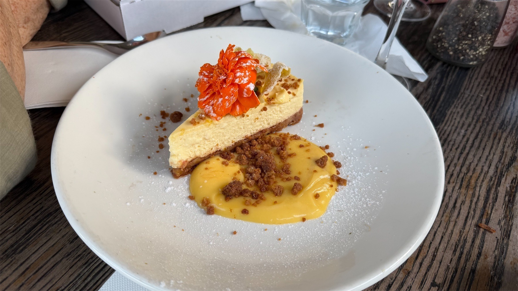 Slice of cheesecake on a white plate and decorated with a red flower. 