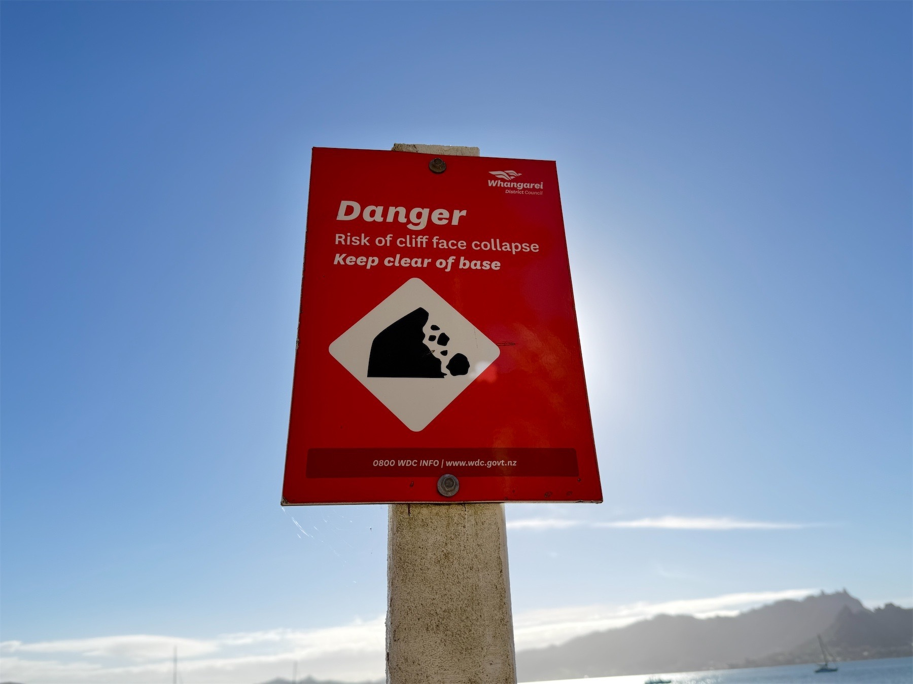 Red sign reading: Danger Risk of cliff face collapse Keep clear of base.