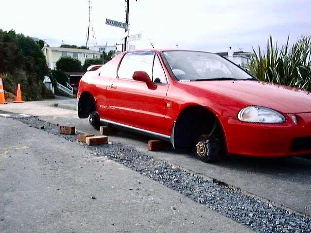 Red sports car propped up on bricks, with no wheels.