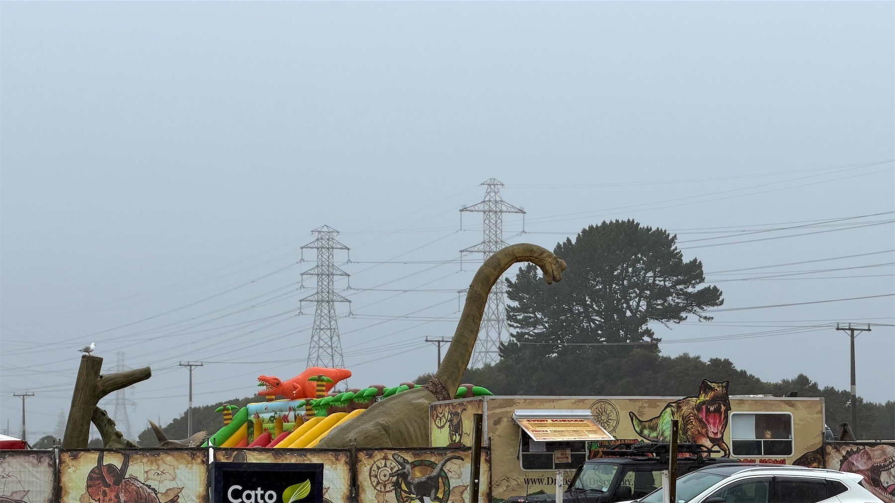 A rainy view of a dinosaur towering over an enclosure. 