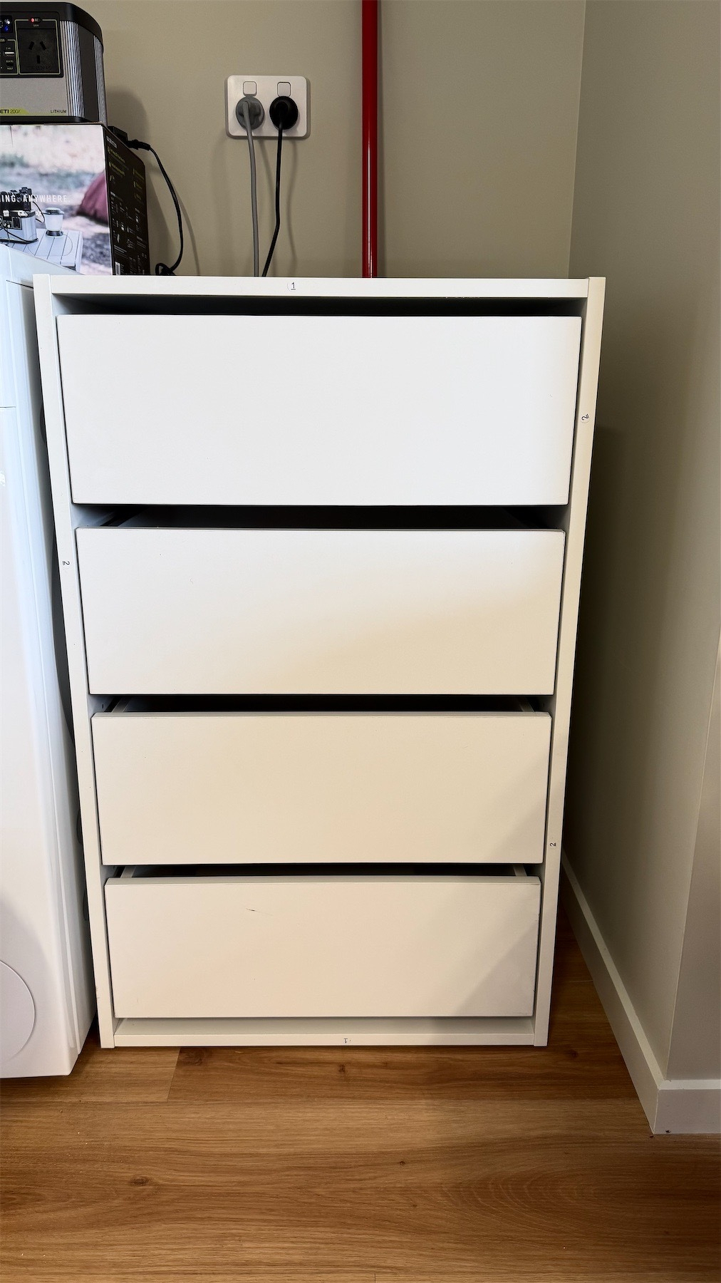 A set of 4 drawers, white, tucked into a small space in the garage.