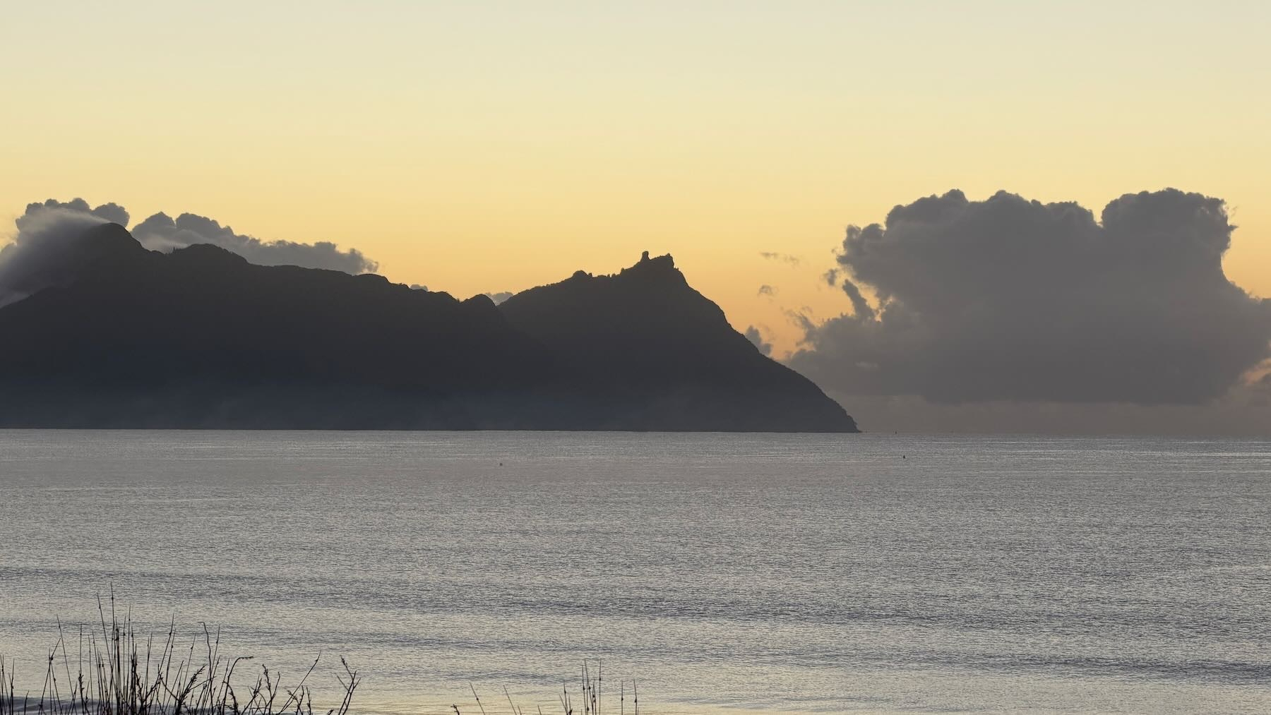 Pale sky with silhouette of a hill, clouds, sea and beach. 