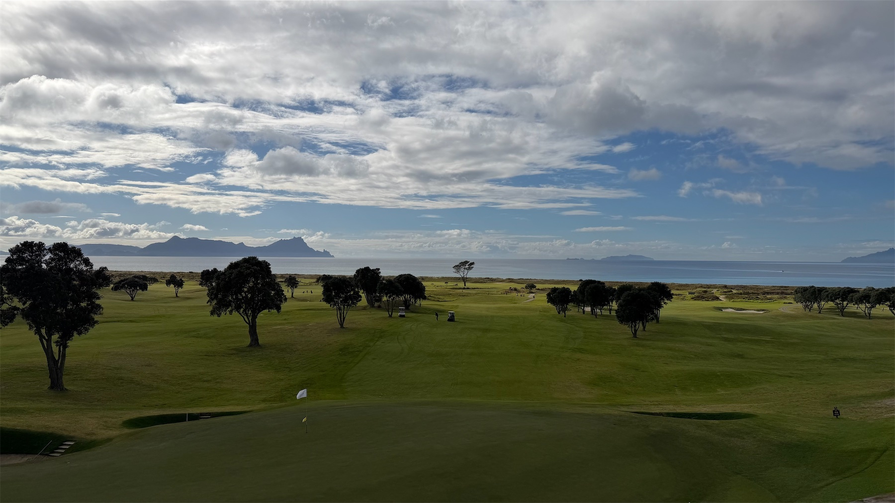 A golf course with scattered trees extends toward a body of water under a partly cloudy sky.
