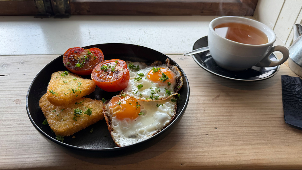 Fried eggs, cooked tomato and hash browns on a black plate. 