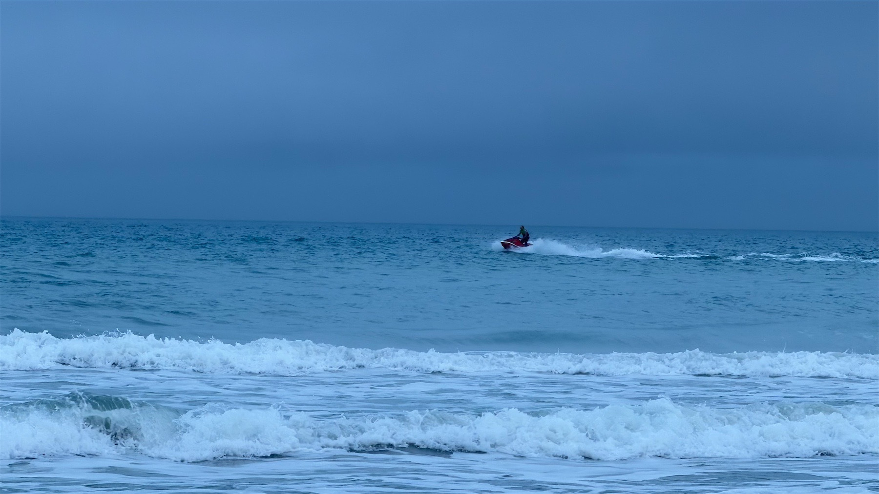 Blue sea; someone on a jetski speeding from right to left. 