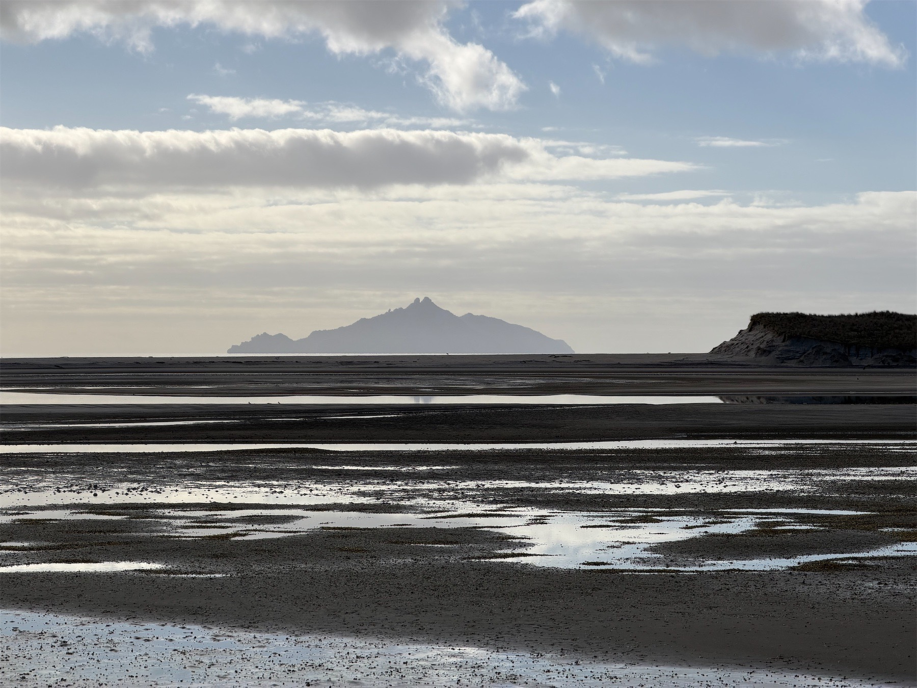 View across wet sand and sea to a distant island. 