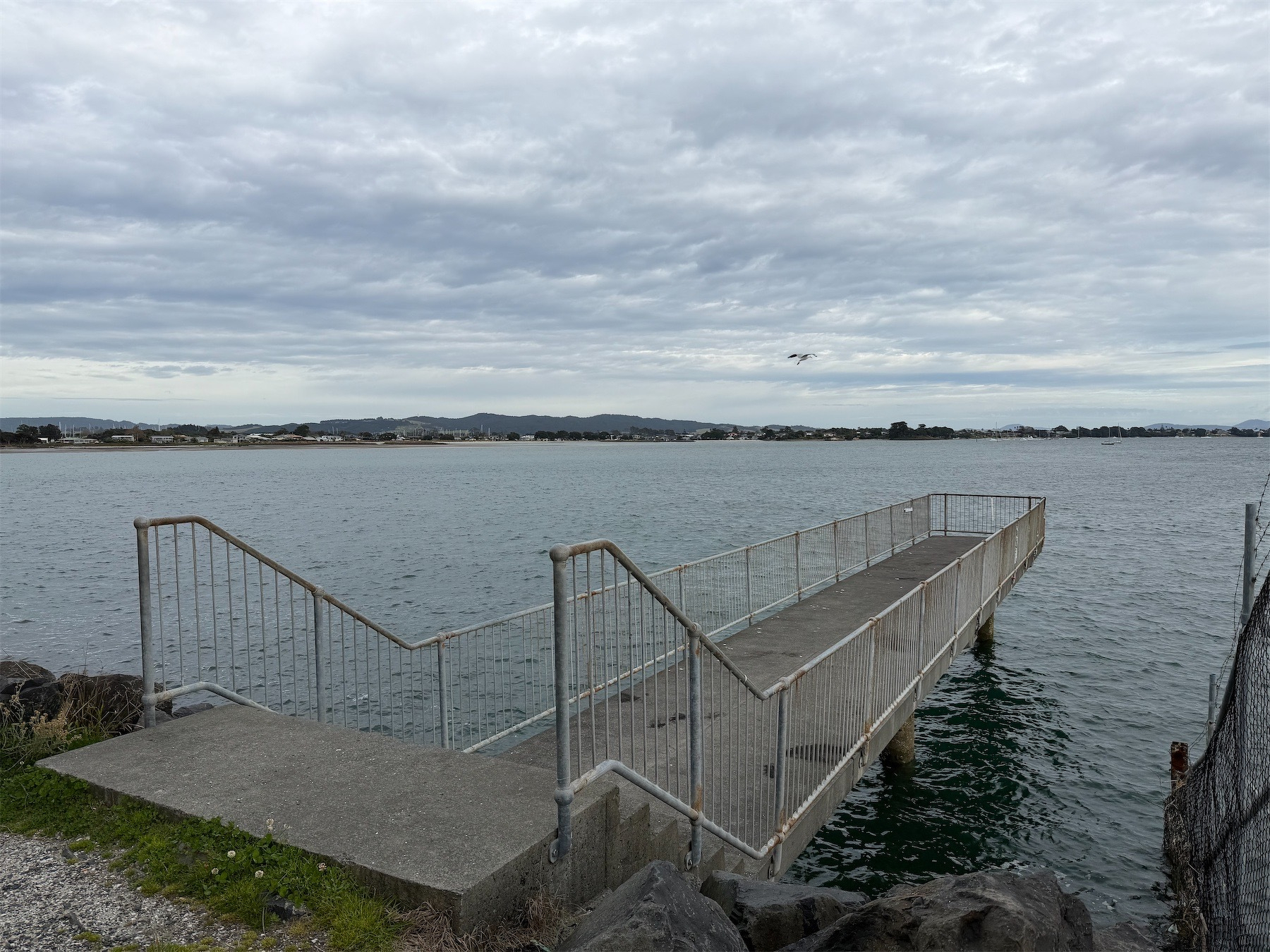 Pier stretches into the sea with land and houses across the bay. 