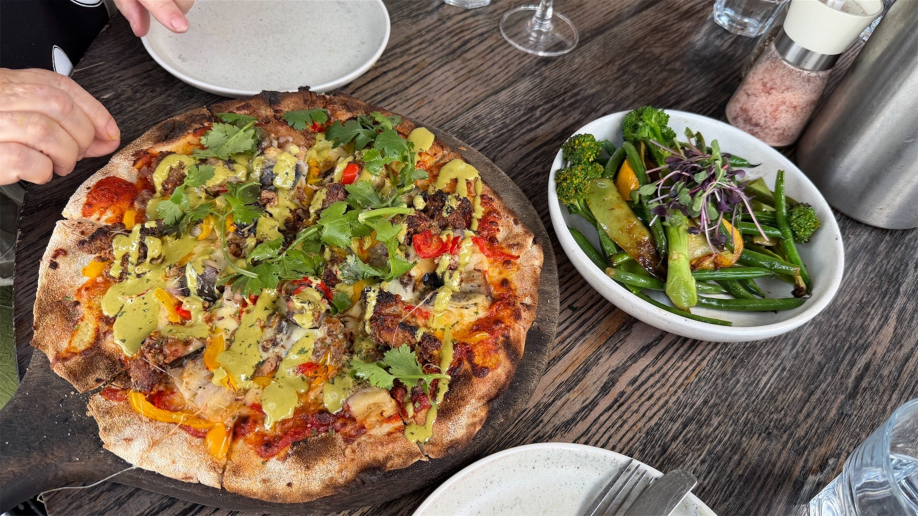 A platter with a loaded pizza beside a dih of cooked green vegetables. 