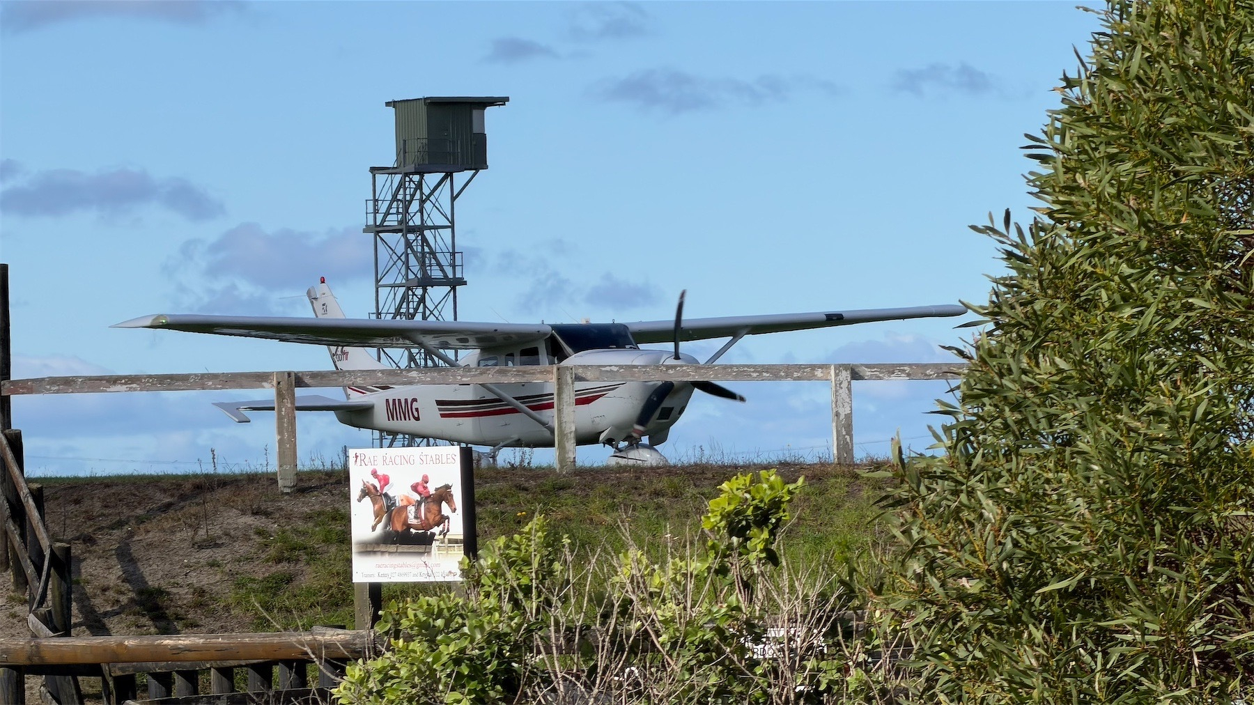 Small plane behind a wooden barrier and with a racecourse announcing tower behind. 