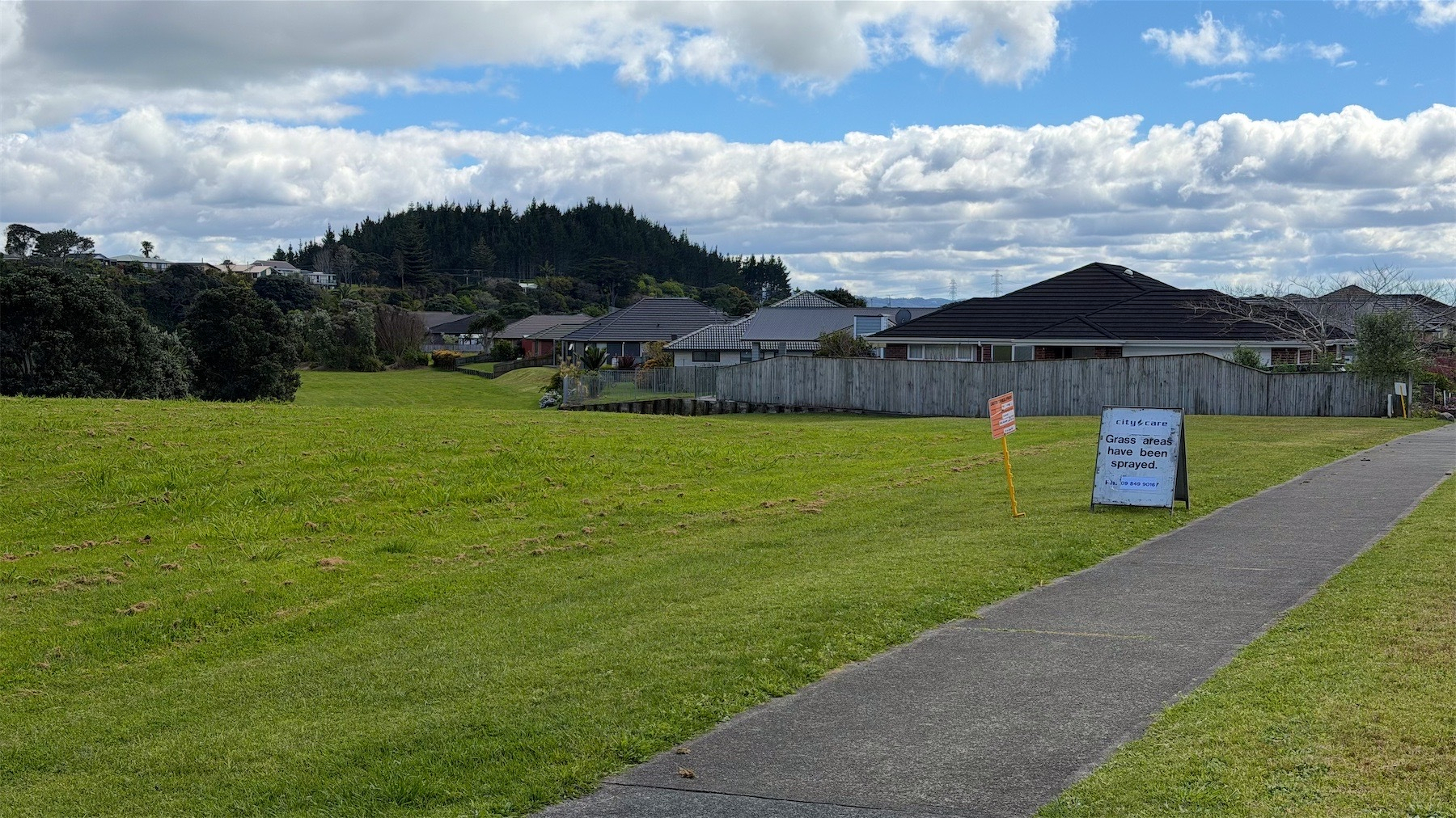 A grassy area beside and behind houses with a white sign reading: Grass Areas have been sprayed.