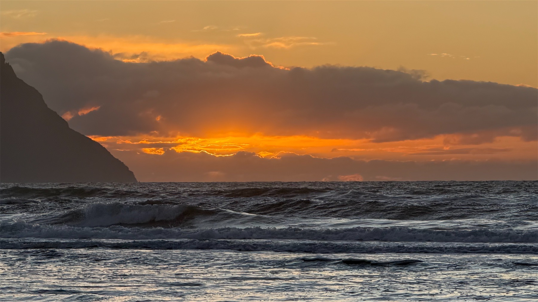Shiny water, a hill on the left and orange peeking through clouds. By the horizon. 