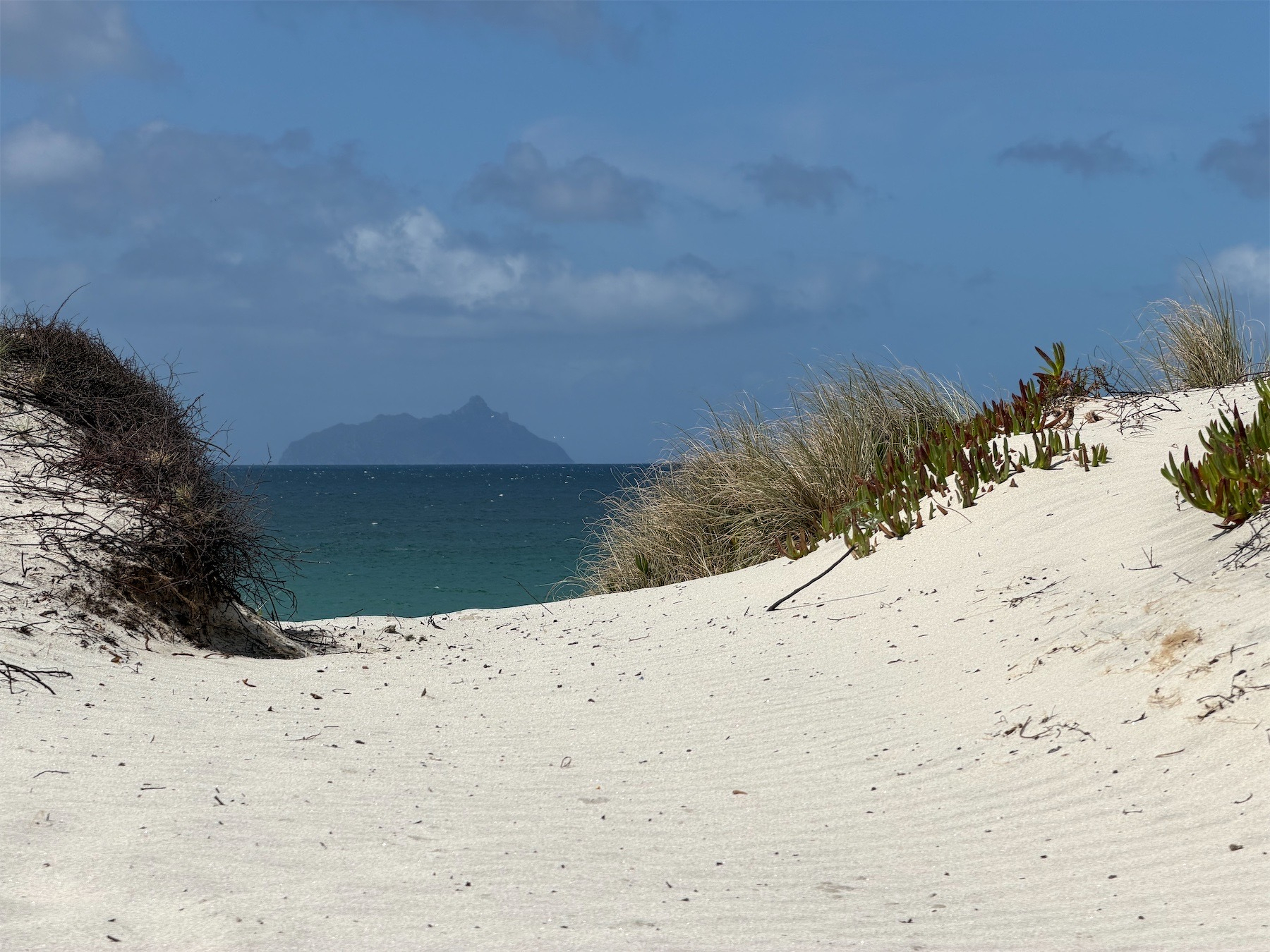 A white sandy track leads to the sea and a large island in the distance. 
