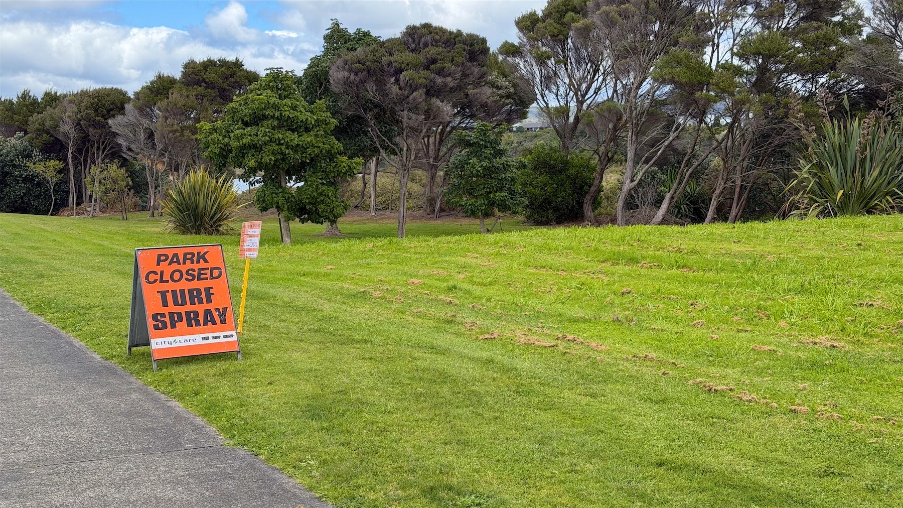 A green grassy area with trees and an orange sign reading: Park Closed Turf Spray. 