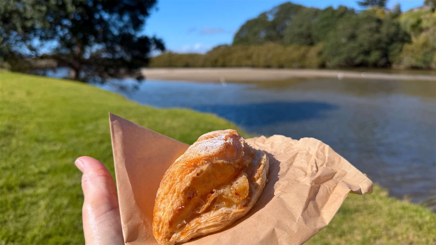 Apple turnover on a hand with river, grass and trees in the background.